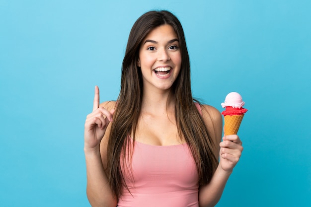 Teenager Brazilian girl holding a cornet ice cream over isolated blue wall pointing up a great idea