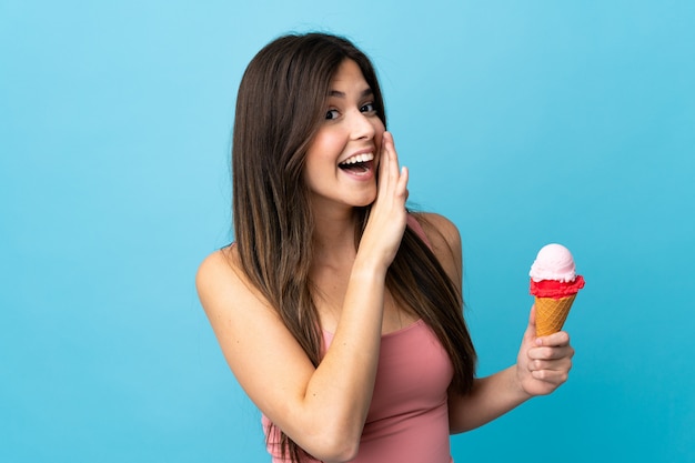 Teenager Brazilian girl holding a cornet ice cream over isolated blue wall whispering something