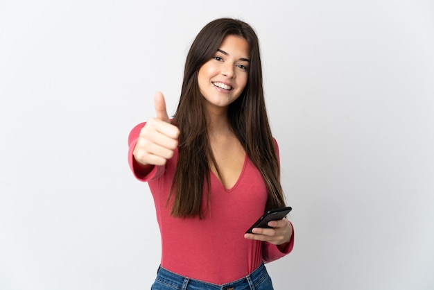 Teenager Brazilian girl isolated on white using mobile phone while doing thumbs up