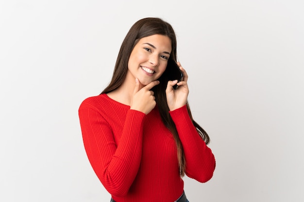 Teenager Brazilian girl using mobile phone over isolated white background happy and smiling