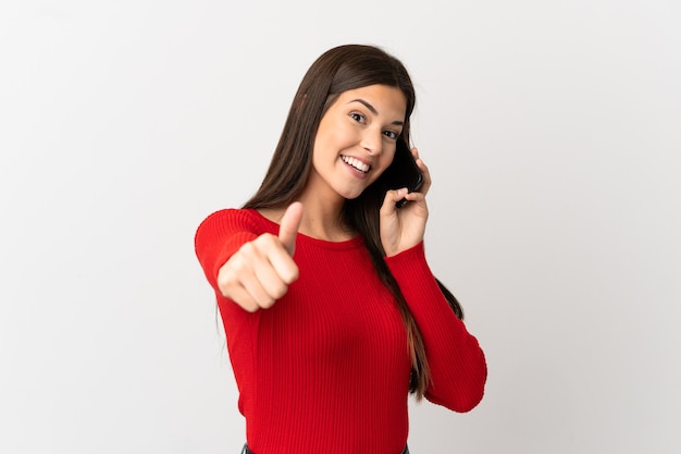 Teenager Brazilian girl using mobile phone over isolated white background with thumbs up because something good has happened