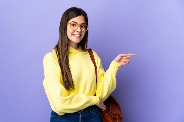 Teenager Brazilian student girl over isolated purple wall pointing finger to the side