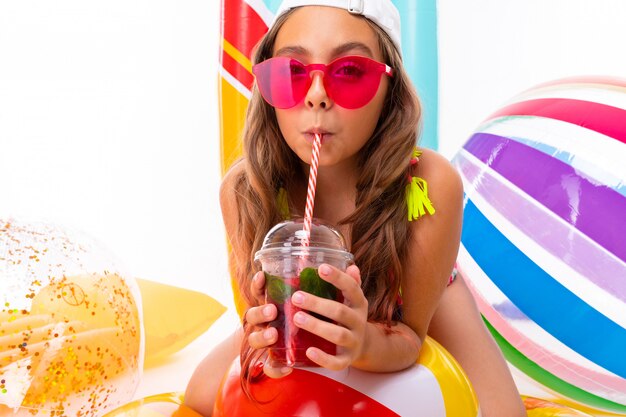 Teenager caucasian girl in glasses with cocatail on white wall