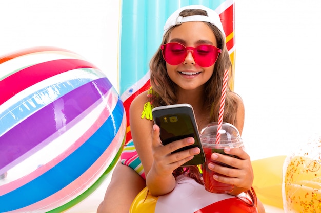 Teenager caucasian girl in glasses with cocatail on white wall