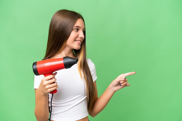 Teenager Caucasian girl holding a hairdryer over isolated background pointing to the side to present a product