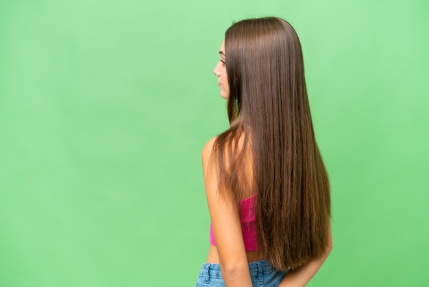 Teenager caucasian girl over isolated background in back position and looking back