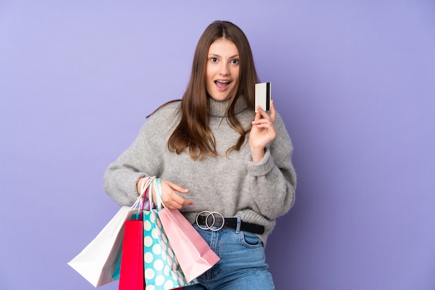 Teenager caucasian girl isolated on purple holding shopping bags and surprised