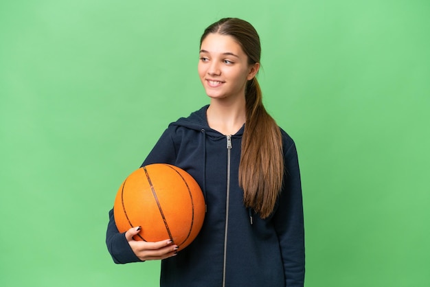 Teenager caucasian girl playing basketball over isolated background looking to the side and smiling