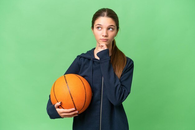 Teenager caucasian girl playing basketball over isolated background and looking up