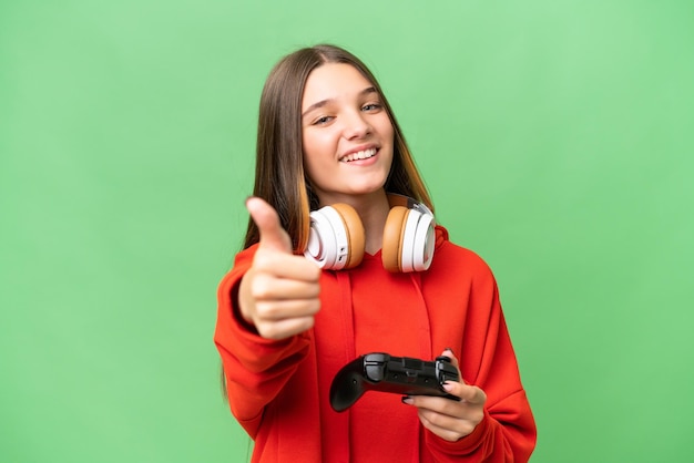 Teenager caucasian girl playing with a video game controller over isolated background with thumbs up because something good has happened