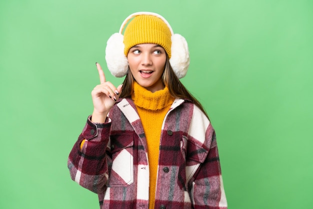 Teenager caucasian girl wearing winter muffs over isolated background intending to realizes the solution while lifting a finger up