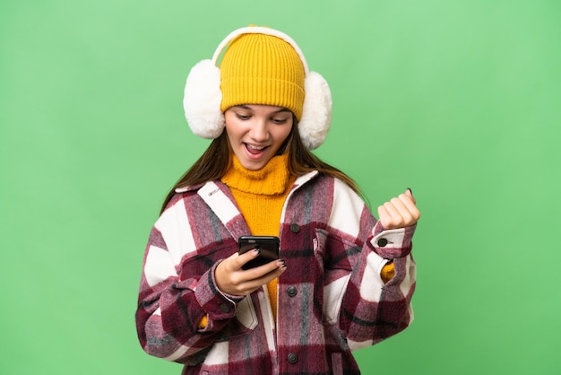 Teenager caucasian girl wearing winter muffs over isolated background surprised and sending a message