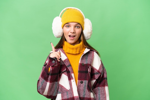 Photo teenager caucasian girl wearing winter muffs over isolated background thinking an idea pointing the finger up