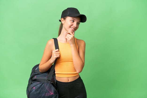 Teenager caucasian girl with sport bag over isolated background thinking an idea and looking side