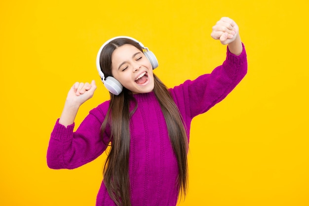 Teenager child girl in headphones listening music wearing stylish casual outfit isolated over yellow background