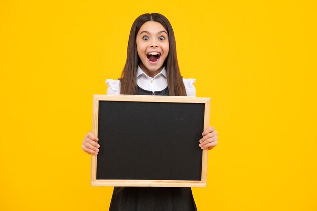 Teenager child holding blank chalkboard for message Isolated on a yellow background Empty text