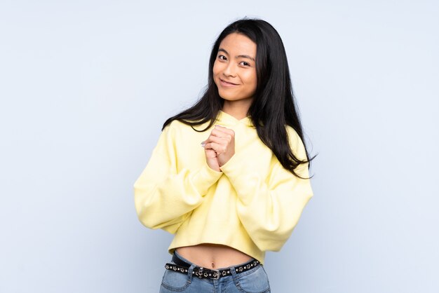 Teenager Chinese woman isolated on blue background laughing