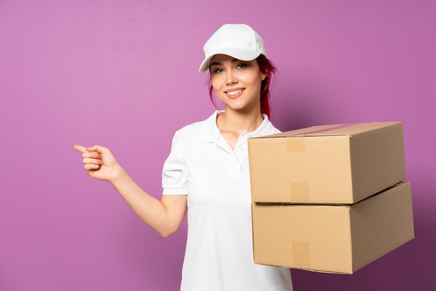 Teenager delivery girl isolated on purple background pointing finger to the side