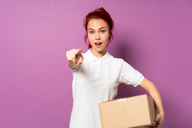 Teenager delivery girl isolated on purple background surprised and pointing front