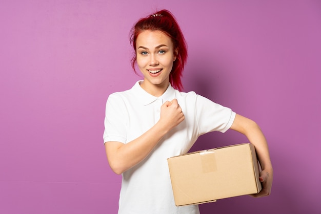 Teenager delivery girl isolated on purple celebrating a victory