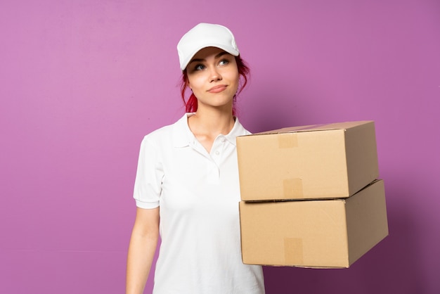 Teenager delivery girl isolated on purple wall and looking up