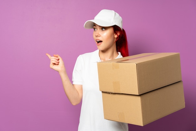 Teenager delivery woman isolated on purple wall intending to realizes the solution while lifting a finger up