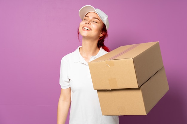 Teenager delivery woman isolated on purple wall laughing