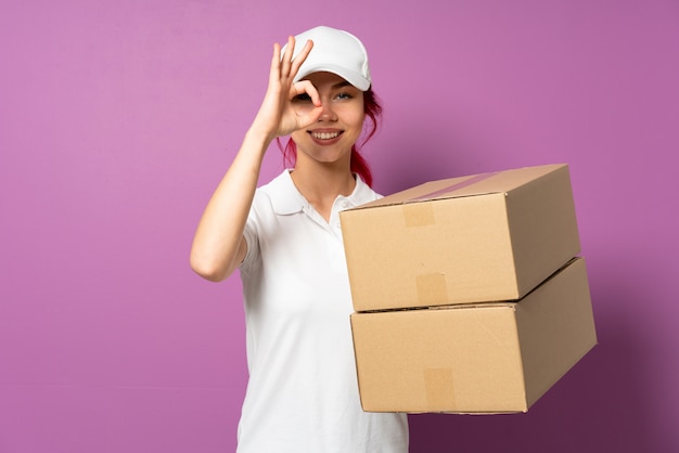 Teenager delivery woman isolated on purple wall showing ok sign with fingers