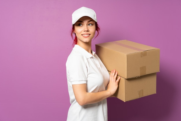 Teenager delivery woman isolated on purple wall with arms crossed and happy