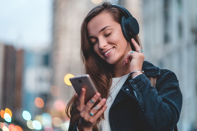 Teenager enjoys and listens to music in black wireless headphones while walking around the city