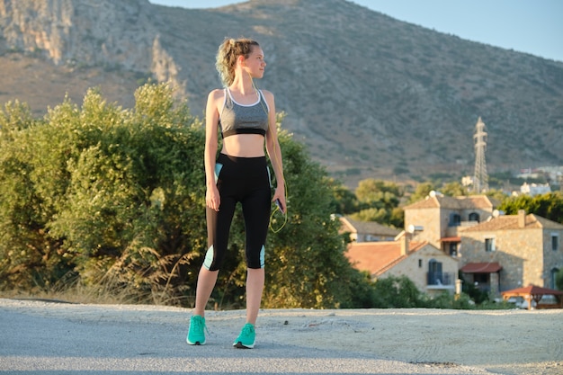 Teenager fitness runner girl in sportswear with smartphone in earphones on mountain