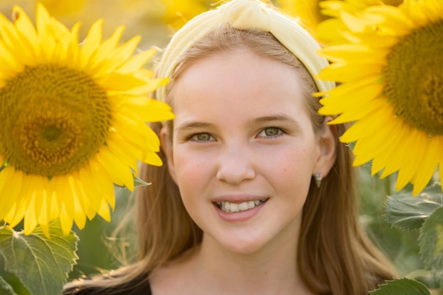 Teenager girl hides behind sunflowers showing toothy smile