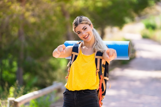 Teenager girl hiking at outdoors points finger at you while smiling