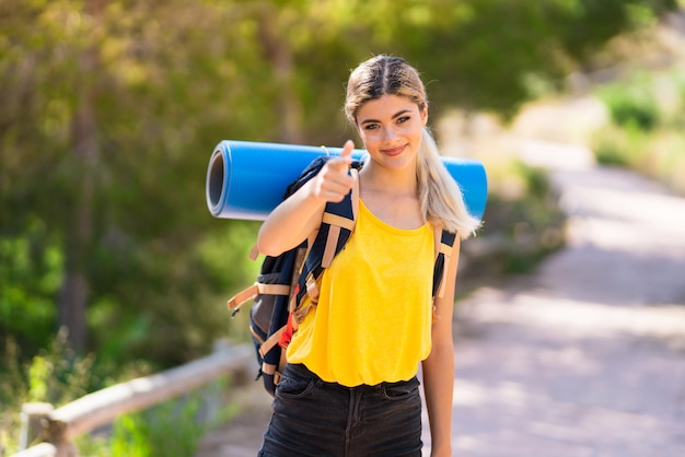 Teenager girl hiking at outdoors points finger at you with a confident expression