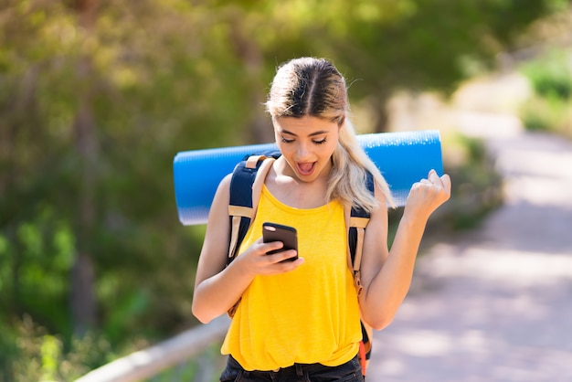 Teenager girl hiking at outdoors surprised and sending a message