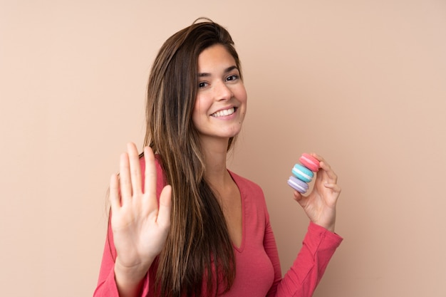 Teenager girl holding colorful French macarons and saluting