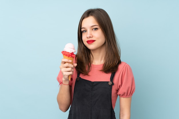 Teenager girl holding a cornet ice cream on blue smiling a lot