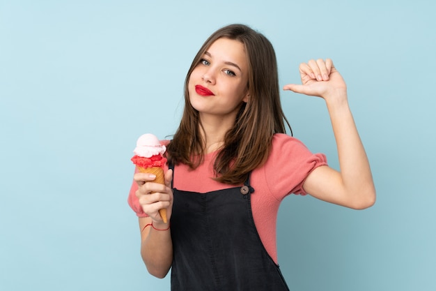 Teenager girl holding a cornet ice cream isolated on blue wall proud and self-satisfied