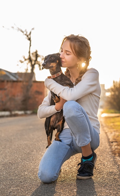 Teenager girl holding her dachshund dog in her arms outdoors in sunset