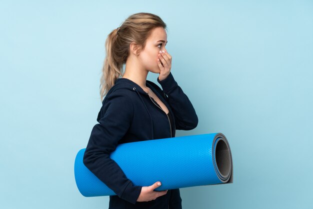 Teenager girl holding mat on blue covering mouth and looking to the side