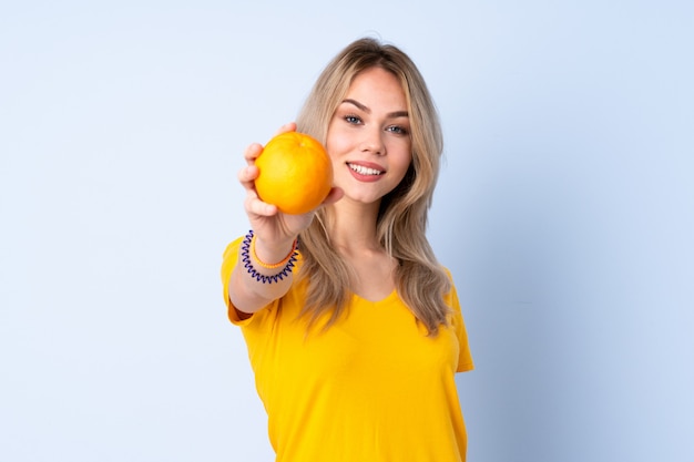 Teenager girl holding an orange on blue wall