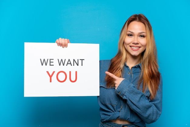 Photo teenager girl over isolated blue background holding we want you board and  pointing it