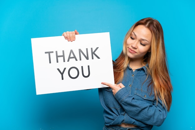 Teenager girl isolated holding a placard with text THANK YOU and  pointing it