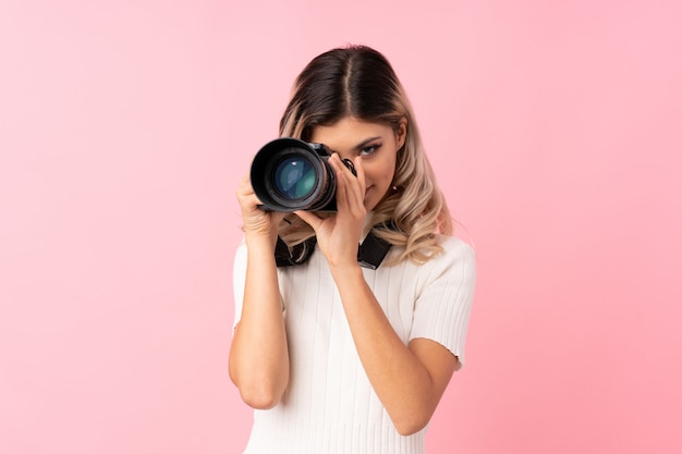 Teenager girl over isolated pink background with a professional camera