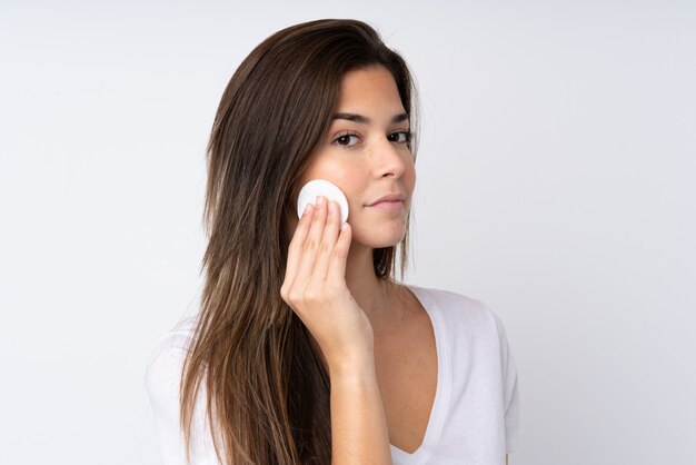 Teenager girl over isolated wall with cotton pad for removing makeup from her face