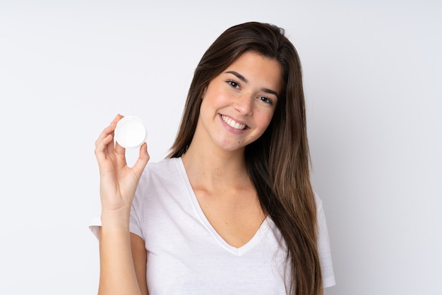 Teenager girl over isolated wall with moisturizer and happiness