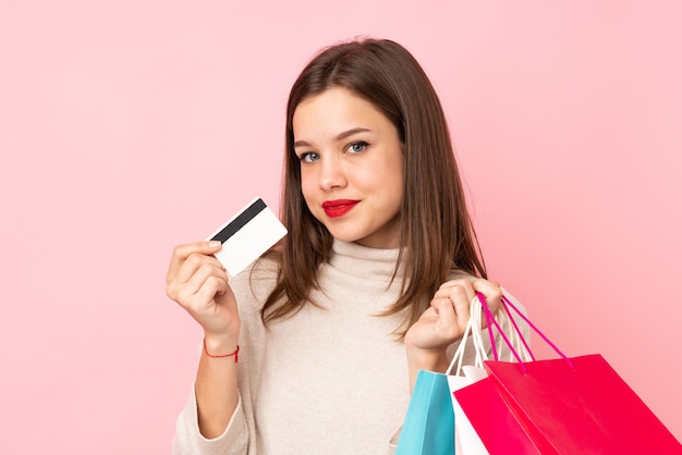 Teenager girl on pink holding shopping bags and a credit card