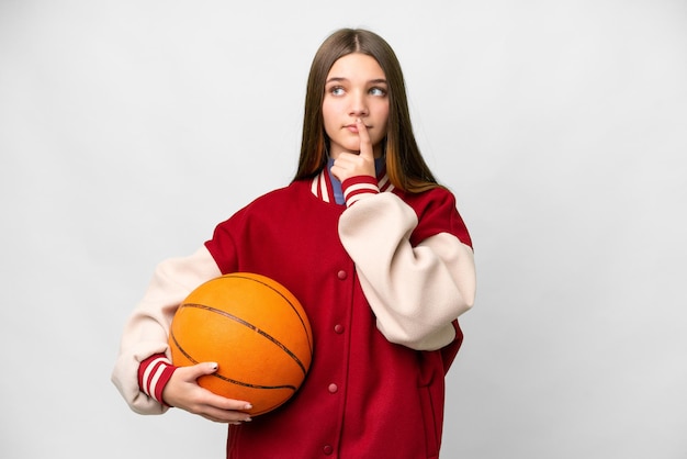 Teenager girl playing basketball over isolated white background having doubts while looking up