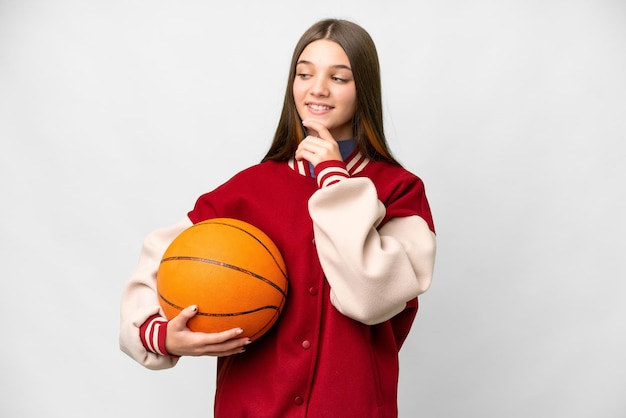 Teenager girl playing basketball over isolated white background looking to the side and smiling