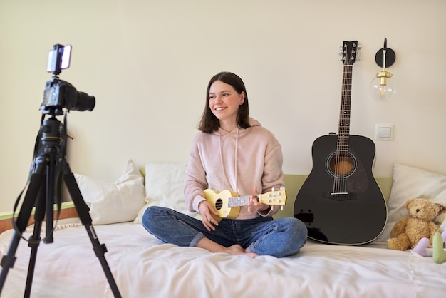 Teenager girl plays music on ukulele, online learning and chatting with followers. Musical teenage blog, vlog, channel, modern technology, youth concept